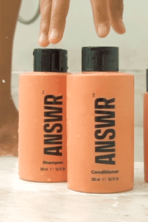 Woman in shower picking up ANSWR’s Shampoo and conditioner